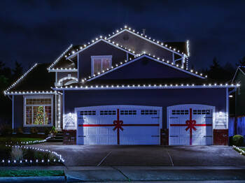 Suburban house at night decorated with Christmas lights and red bows on the garage doors