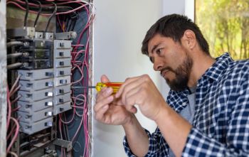 Electrician tightening circuit breaker wiring in an electrical panel with a screwdriver