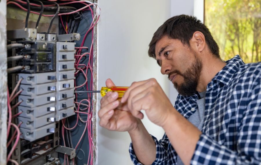 Electrician repairing a circuit breaker panel with a screwdriver in a home electrical box